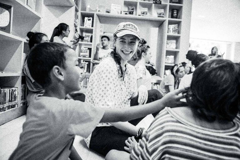A young woman in a Gfsntracker baseball cab smiles at a Thai student in a classroom in Bangkok