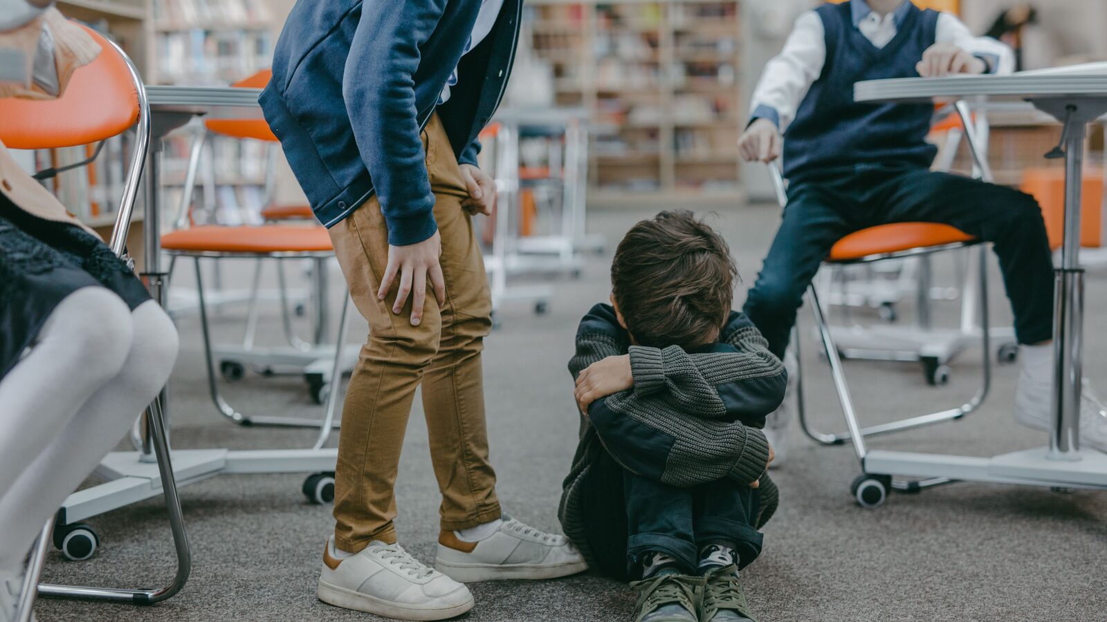 A young child sitting on the floor in a classroom facing bullying from peers.